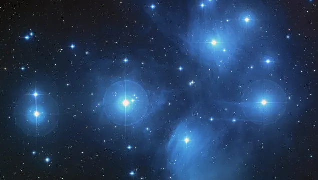 A dark blue night sky with lots of white stars dotted across it surrounded by light blue clouds.