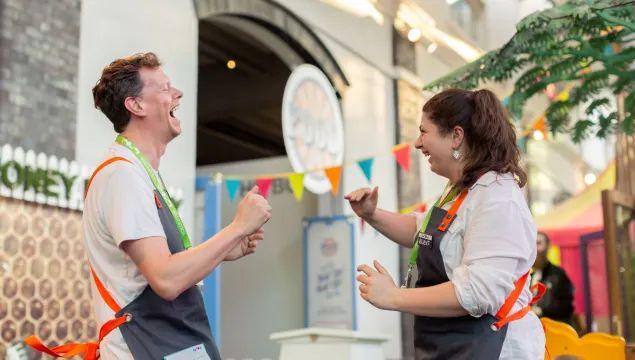 Two volunteers wearing grey aprons looking at each other and laughing