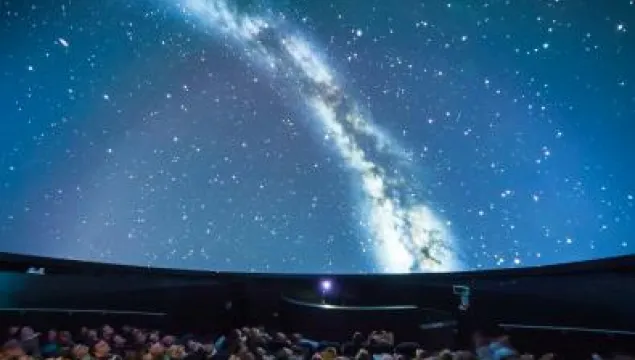 Inside of a planetarium.  The room is full of people looking up at a dome showing the edge of the galaxy.