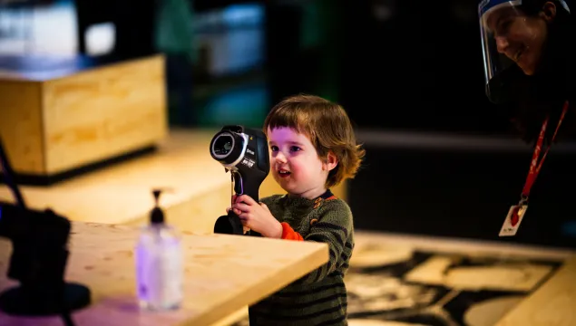 A small child is in the middle of a wooden space holding up a camera device.