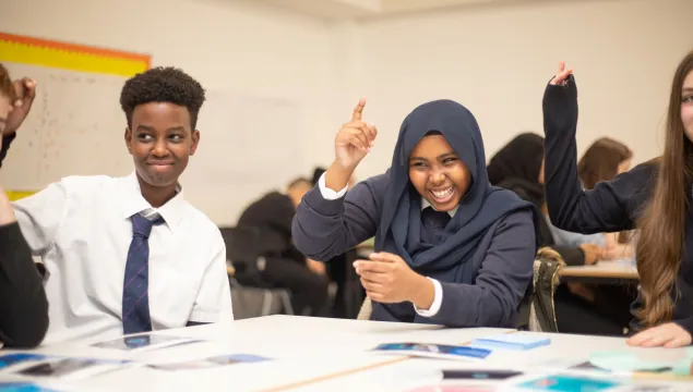 Students around a table smiling and raising their hands