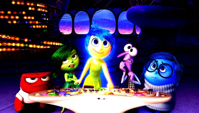 Promotion picture for the animated film Inside Out featuring the main character Ryle standing behind a table surrounded by animated figures representing her emotions 