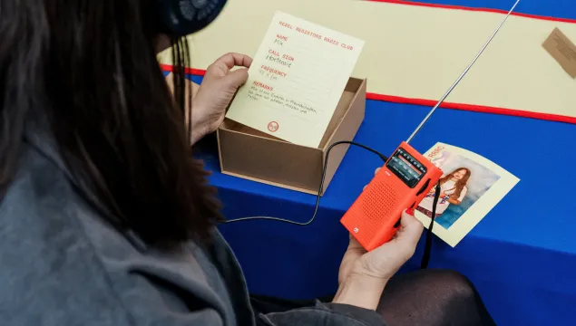 A person is sat at a desk holding an old radio and a piece of paper.