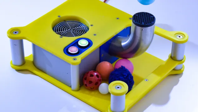 A portable exhibit which has a blue ball floating above a pipe and a selection of other balls nearby