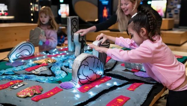 A group of people are in the middle of a science centre playing with a soft playable map.