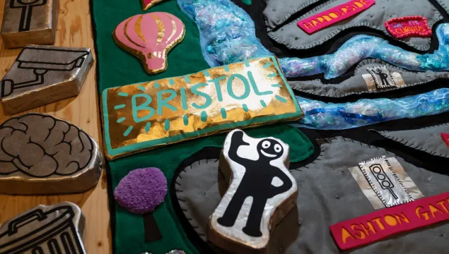 A colourful handcrafted collage with raised icons, including a “BRISTOL” sign, a hot air balloon, a waving Morph figure arranged on a textured map-like background