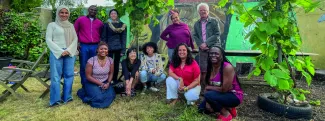 A group of people in front of some plants, together for a photo. Some are crouched, some are stood up.