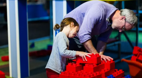 An adult and child working together with giant red building bricks