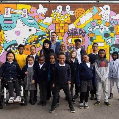 Hannah More school pupils and their headteacher stood in front of a colourful mural. Image credit Freia Turland