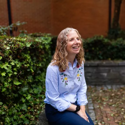 Person with shoulder length wavy hear smiling in a courtyard 