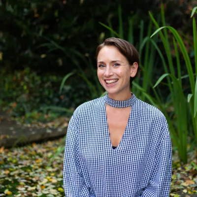 A smiling person with a brown bob haircut sitting in front of green plants looking at the camera