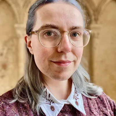 Portrait head shot of a person with shoulder length grey blonde hair and glasses 