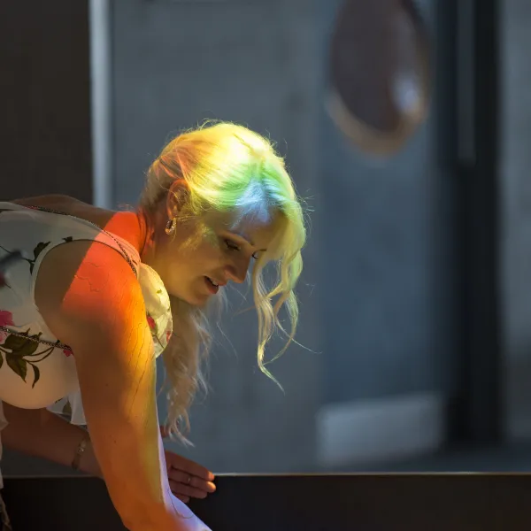 A woman in a formal dress interacting with an exhibit. Rainbow light is projected onto her. 