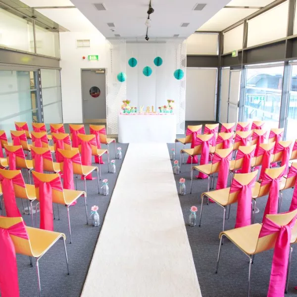 A decorated room arranged for a wedding ceremony, with an aisle and chairs set up either side. 