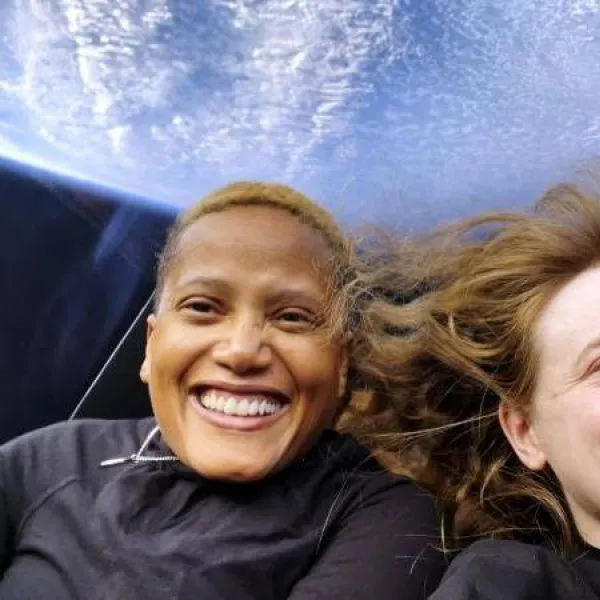 Two female astronauts in space with the Earth behind them.  They are both smiling a lot.