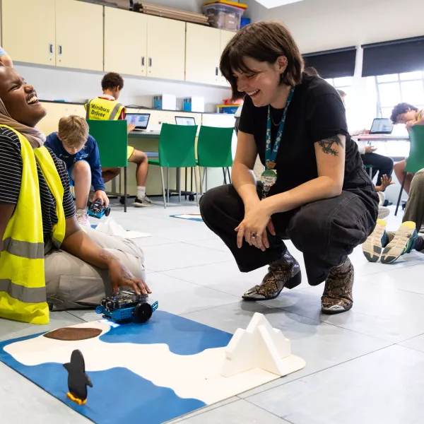 A member of staff and school pupil sat on the floor in a classroom environment. They are both laughing together next to a model of an arctic environment