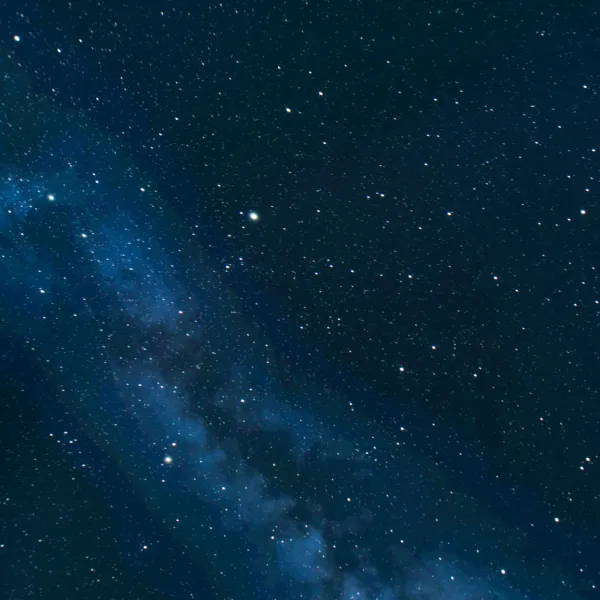 A dark blue night sky with lots of white stars dotted across it, and a lighter blue cloud in the left-hand side of the image.