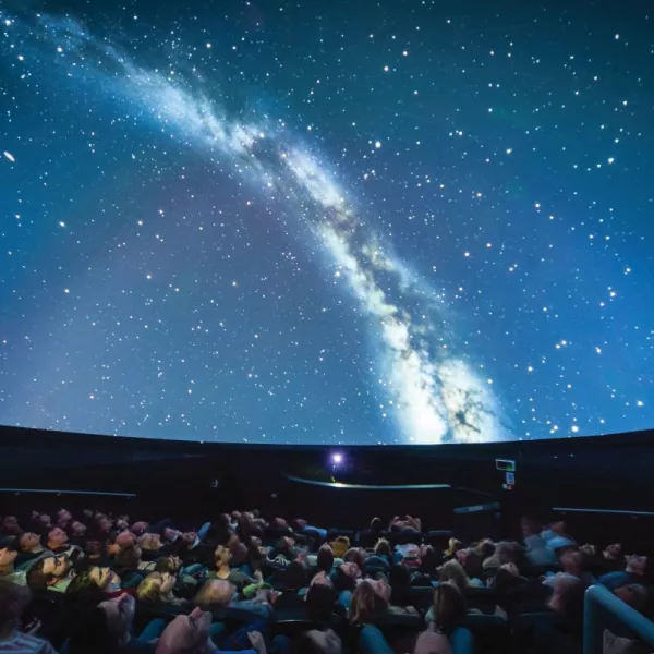 Audience in a planetarium watching a projection of the Milky Way galaxy on the dome-shaped ceiling.