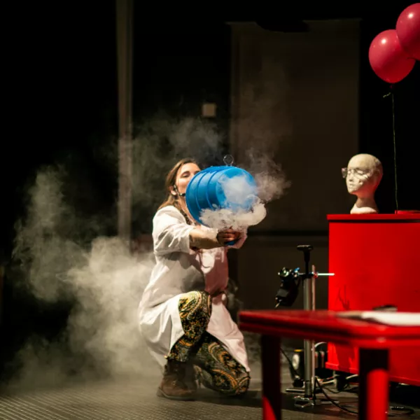 We The Curious staff member holding a big blue barrel with smoke coming out of it in a studio science show for schools