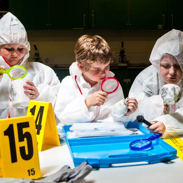 Three children in white coveralls looking at different objects with magnifying classes in a DNA detectives workshop