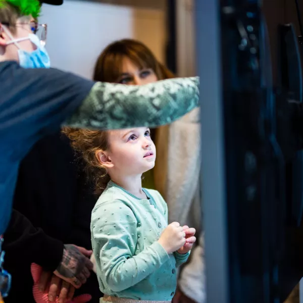 A young child is looking up at a digital screen, which a We The Curious member staff is pointing to 