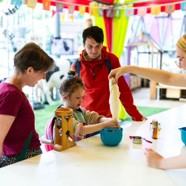 A child and two adults in the Kitchen at We The Curious. The child is being helped to make oat milk by a member of staff.