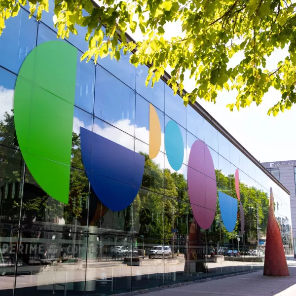 The glass exterior of We The Curious, which has large coloured letters spelling 'Curious'. Branches of a tree are visible in the foreground.