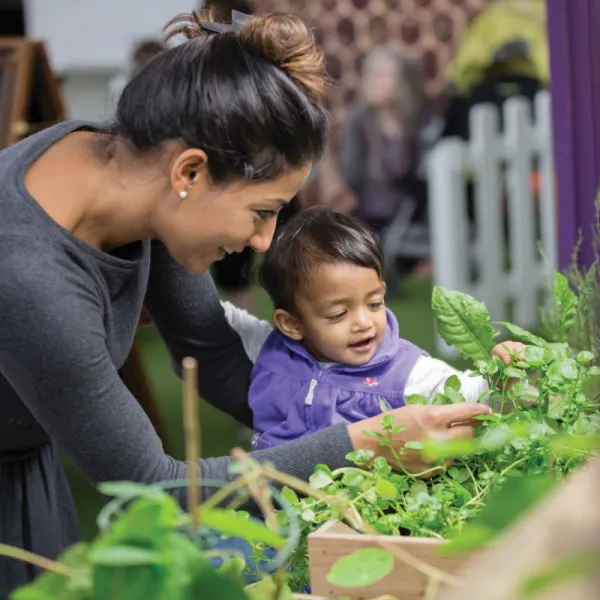 A person smiling and investigating plants with a toddler in the greenhouse exhibit 