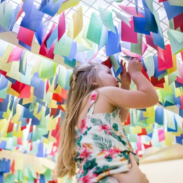 A child being lifted high up to be able to look at colourful tags filled with questions