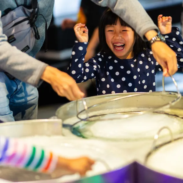 A child looking ecstatic while a grown-up next to them is making a giant bubble