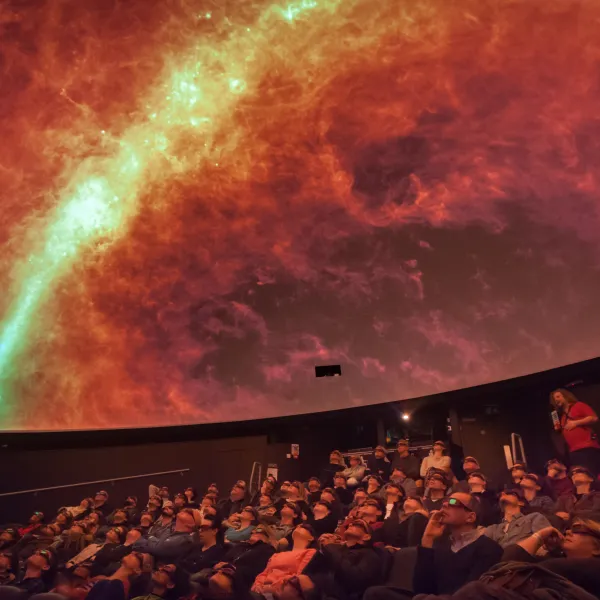 People sat in a planetarium looking up at a red sky projected on the dome.