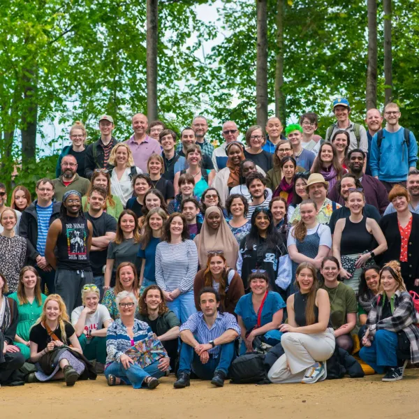 A large group photo featuring approx 100 people looking towards the camera, with green trees behind them