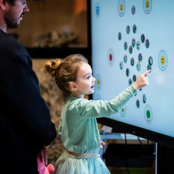 A child in a light green outfit pointing at a digital screen with lots of circular shapes