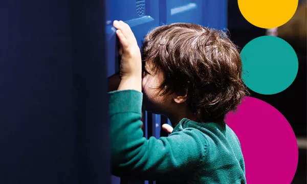 A young child in a green jumper with their face pressed up against the TARDIS, looking through a peep hole. 